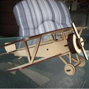 May include: A wooden biplane model with a light brown body and dark brown accents. The model features a propeller, wheels, and a detailed wing structure. The toy plane is a decorative item.