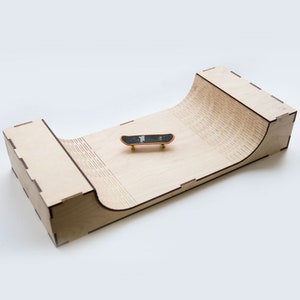 Puede incluir: Una rampa de fingerboard de madera con un fingerboard negro y naranja en la parte superior. La rampa está hecha de madera contrachapada y tiene un diseño curvo.