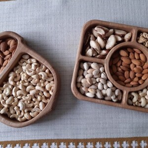 May include: Two wooden serving trays with compartments filled with various nuts, including almonds, cashews, pistachios, walnuts, and Brazil nuts.