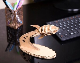 Op de afbeelding: Een kartonnen model van een raket met een gebogen basis en een gelaagd ontwerp. De raket heeft een puntige neus en vinnen, met cirkelvormige details langs de romp. Het model is gemaakt van golfkarton en staat op een zwart oppervlak.