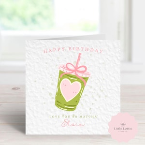 K&ouml;nnte beinhalten: Quadratische Geburtstagskarte mit einer Illustration eines gr&uuml;nen Matcha-Getr&auml;nks, einem rosa Herz und einer rosa Schleife. Die Karte tr&auml;gt die Aufschriften "Happy Birthday" und "Love You So Matcha" mit einem Namen darunter. Das Little Lottie-Logo befindet sich unten rechts.