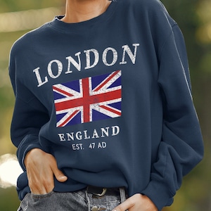 Peut inclure: Un sweat-shirt bleu marine avec un graphique vintage du drapeau britannique et le texte "LONDON ENGLAND EST. 47 AD".