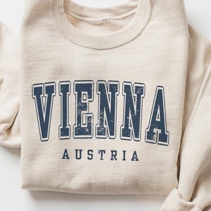 May include: A beige sweatshirt with a navy blue vintage-style graphic that says "VIENNA AUSTRIA".