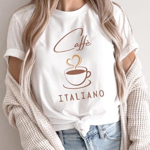 Può includere: Maglietta bianca con la scritta "Caffe Italiano" e un'immagine di una tazza di caffè fumante.