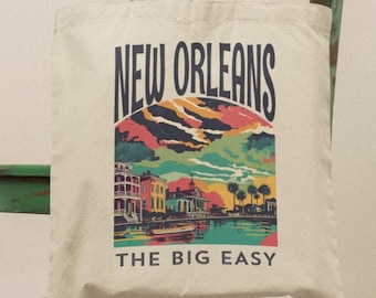 Puede incluir: Un bolso de tela color crema con un estampado gráfico colorido de la arquitectura de Nueva Orleans y un cielo al atardecer. El texto NEW ORLEANS aparece en una fuente arqueada azul oscuro sobre la escena, con THE BIG EASY impreso debajo en azul.