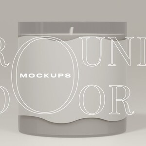 Peut inclure: Un bocal rond en verre pour bougie avec une étiquette blanche sur laquelle est inscrit "MOCKUPS" et une bougie en cire blanche à l'intérieur. Le bocal est posé sur une surface gris clair. Les mots "ROUND" et "DOOR" sont écrits en blanc autour du bocal.