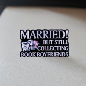 May include: Black enamel pin with white text that reads "Married! But still collecting book boyfriends". The pin features a white open book with a pink bookmark and a small pink heart.