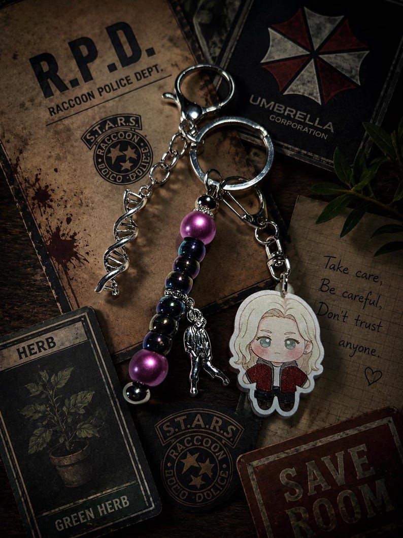 May include: A keychain featuring a silver-toned DNA helix charm, a strand of iridescent dark purple and magenta beads, a small silver figure charm, and a flat acrylic charm depicting a blonde character in a red jacket and black shirt.