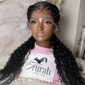 May include: A black curly wig with braided details and a lace front, displayed on a mannequin head. The mannequin wears a pink and white top with the text "Aurah Luxe Hair". White flowers are placed on the head.