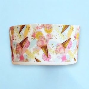 May include: A white container with a repeating pattern of pink ice cream cones, lemon slices, and pink citrus fruit. The design includes yellow, pink, and blue brushstrokes, with gold glitter accents. The container is likely for holding items.