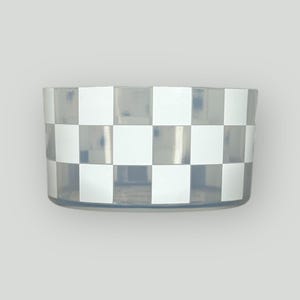 May include: A clear, cylindrical container with a white and gray checkered pattern around the exterior. The container is made of a transparent material, allowing visibility of the contents. The design is a classic checkerboard.