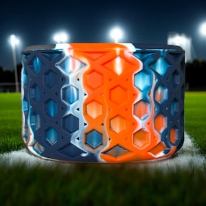 May include: A blue, white, and orange patterned silicone ring with a honeycomb design. The ring is on a green grassy surface.