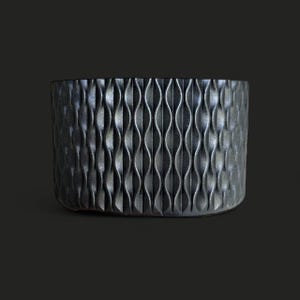May include: A dark grey, cylindrical planter with a textured, wave-like pattern. The planter has a rounded base and a smooth rim. The design is modern and minimalist, suitable for indoor or outdoor use.