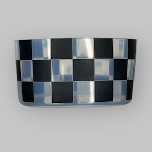 May include: A clear, rectangular container with a black and white chequered pattern. The container has a slightly curved shape and is likely made of glass or a similar transparent material. The design is reminiscent of a racing flag.