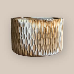 May include: A white and gold ceramic planter with a wavy, textured design. The planter is round and has a smooth, glossy finish.