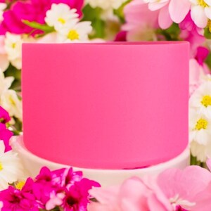May include: A bright pink silicone ring, perfect for holding a cup or mug. The ring is sitting on a white surface surrounded by pink and white flowers.