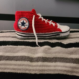 May include: A handmade red and white crochet high-top sneaker with white laces. The sneaker features a Converse All Star patch on the side. The sole is white with black and gray stripes. A unique, handcrafted item.