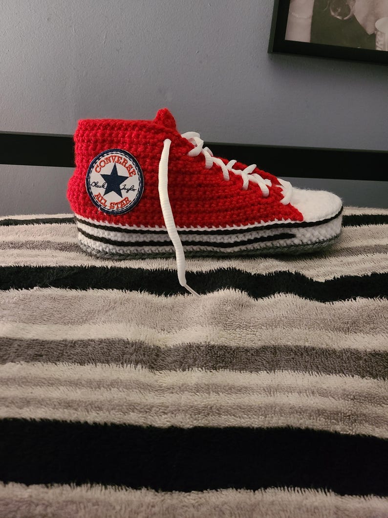 May include: A handmade red and white crochet high-top sneaker with white laces. The sneaker features a Converse All Star patch on the side. The sole is white with black and gray stripes. A unique, handcrafted item.