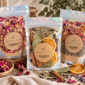 May include: Three iridescent stand-up pouches filled with dried botanicals. Each pouch features a round tan label with the text "wb DIY WILD BOTANICALS". The contents include dried rose petals, orange slices, cinnamon sticks, and herbs.