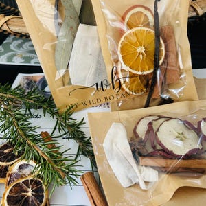 K&ouml;nnte beinhalten: Drei transparente Plastikt&uuml;ten gef&uuml;llt mit getrockneten Fr&uuml;chten, Gew&uuml;rzen und Kr&auml;utern zum Herstellen eines DIY Wild Botanical Simmer Pots. Die Beutel sind mit "DIY WILD BOTANICALS" beschriftet.