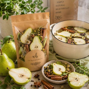 May include: A brown paper pouch labeled DIY WILD BOTANICALS containing dried pear slices, cinnamon sticks, and herbs. Beside it, a white pot holds simmering liquid with pear slices and spices, while a bowl contains similar dried ingredients.