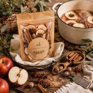 May include: A kraft paper pouch labeled DIY Wild Botanicals containing dried apple slices, cinnamon sticks, and star anise. The pouch sits in a wire basket with a white cloth, surrounded by fresh apples, whole nutmeg, a wooden scoop, and a metal grater.