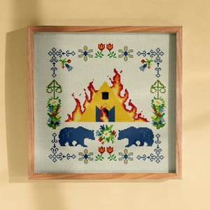 May include: A framed cross-stitch embroidery depicting a yellow house engulfed in flames, with two blue bears on either side. The house is surrounded by a border of flowers and other floral motifs.