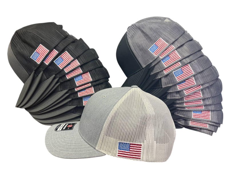 May include: A collection of baseball caps in various shades of gray and black, each featuring an embroidered American flag patch. The caps have a structured design with a mesh back for breathability.