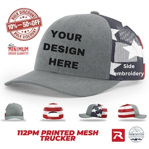 May include: A grey trucker hat with a mesh back featuring a white star pattern on a blue background and red stripes. The front panel displays the black text YOUR DESIGN HERE. Additional views show the hat from the back and sides with flag motifs.