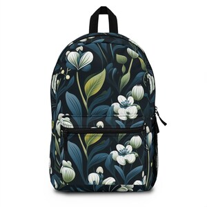 Può includere: Uno zaino con sfondo blu navy scuro e motivo floreale. Il motivo presenta fiori bianchi, foglie blu e accenti verdi e gialli. Lo zaino ha un manico nero, una tasca frontale e una tasca laterale in rete.