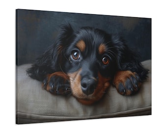 May include: A canvas print of a dog with black and tan fur, and large brown eyes. The dog is resting its paws on a light-coloured cushion, against a dark background. The image is a close-up.