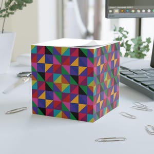 May include: A colorful notepad with a geometric pattern of triangles in shades of red, blue, green, yellow, orange, and purple. The notepad is on a white surface.