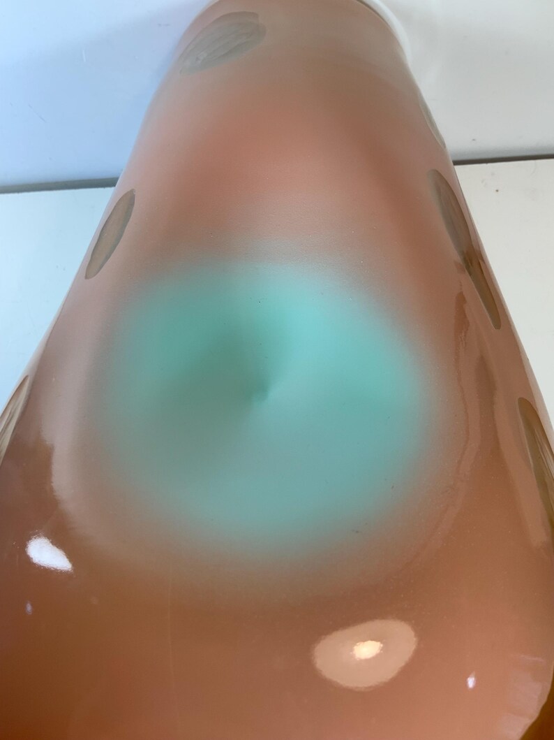 May include: A tall, cone-shaped vase with a gradient of colors. The top is a light peach, transitioning to a turquoise center, and then back to peach. Brownish-gray spots are scattered across the surface. The vase has a glossy finish.