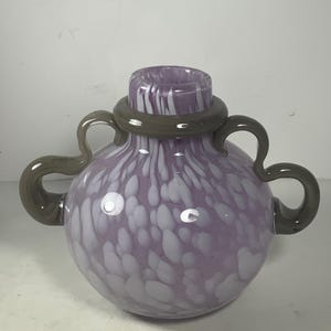 May include: A purple glass vase with white speckles and a grey rim. The vase has two handles on the sides.
