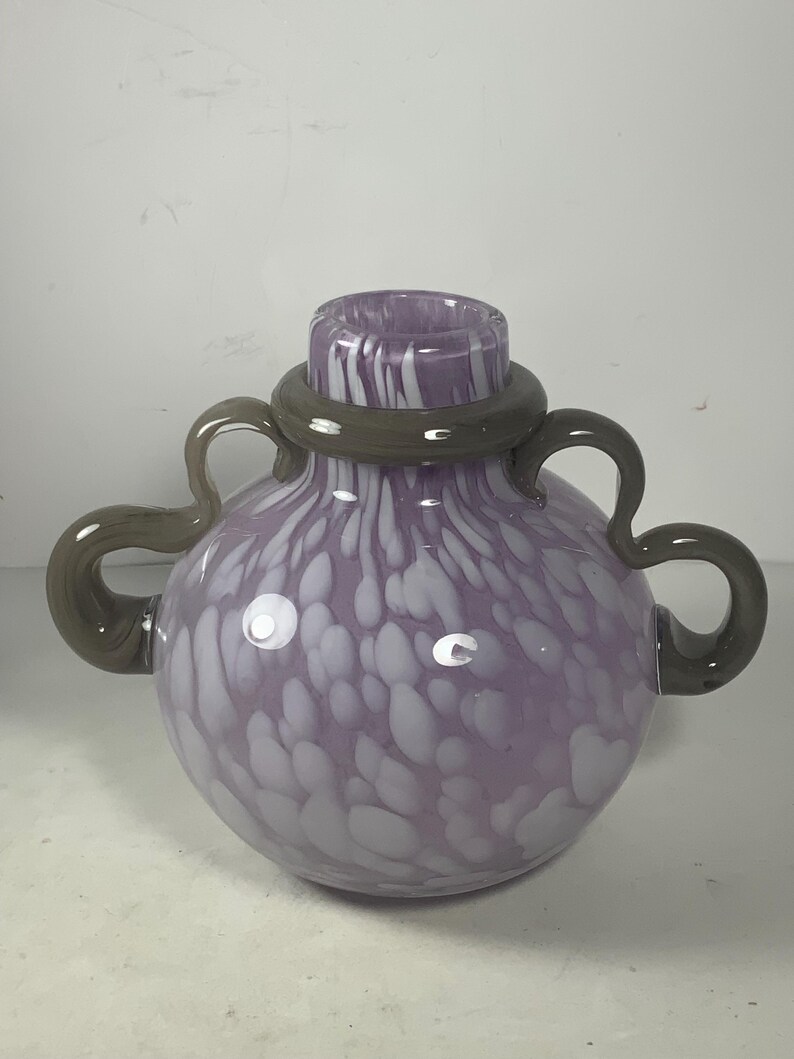 May include: A purple glass vase with white speckles and a grey rim. The vase has two handles on the sides.