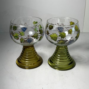 Könnte beinhalten: Zwei klare Weingläser aus Glas mit grünen und blauen Weinreben-Designs. Die Gläser haben einen grünen, gerippten Stiel.