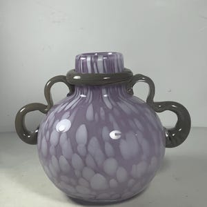 May include: A purple glass vase with white speckles and a grey swirl around the neck. The vase has two grey handles.