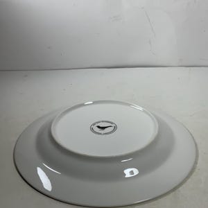 May include: White ceramic dinner plate with a black bird logo on the bottom. The logo reads "The Bird & The Bear, Handcrafted Ceramics, Designed & Made in California".