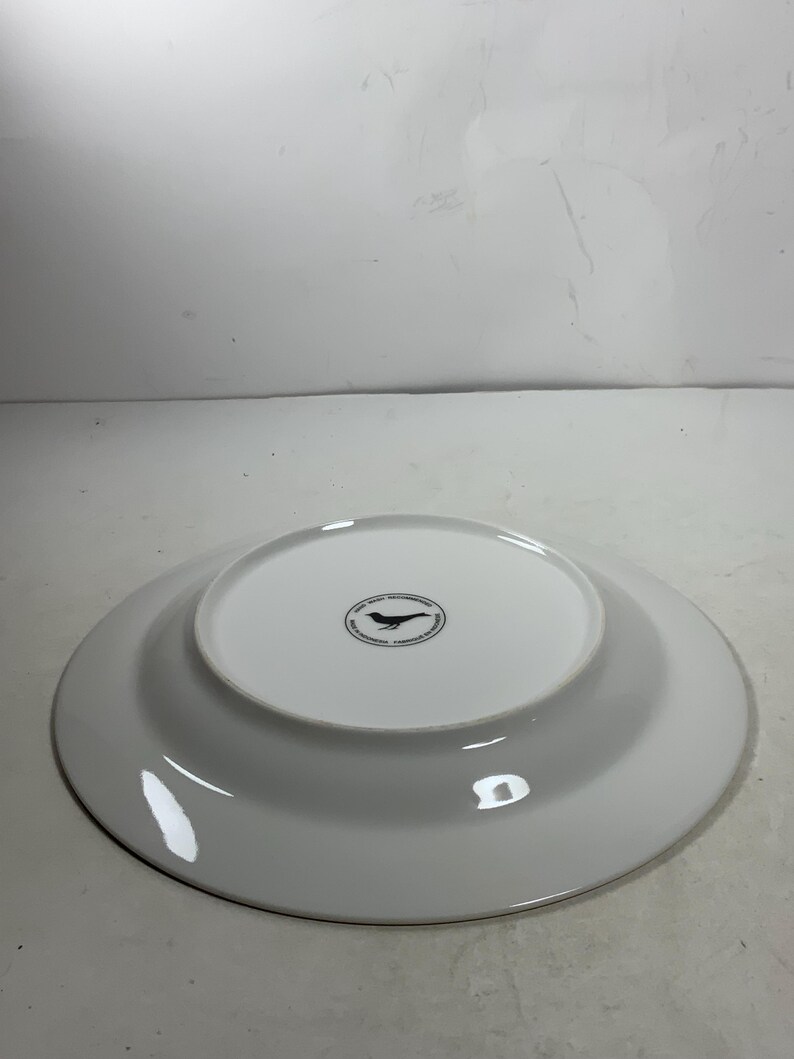 May include: White ceramic dinner plate with a black bird logo on the bottom. The logo reads "The Bird & The Bear, Handcrafted Ceramics, Designed & Made in California".