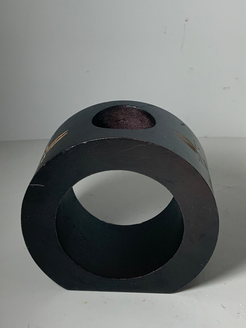 Puede incluir: Un anillo de madera negro con un peque&ntilde;o agujero en la parte superior. El anillo tiene un acabado liso y pulido y est&aacute; decorado con un dise&ntilde;o dorado.