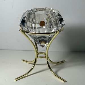 May include: A crystal diamond-shaped candle holder with a gold metal stand. The stand has three legs and a round base.