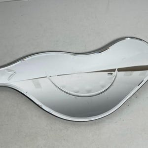 May include: A silver, bird-shaped, decorative mirror with a rounded, curved shape.