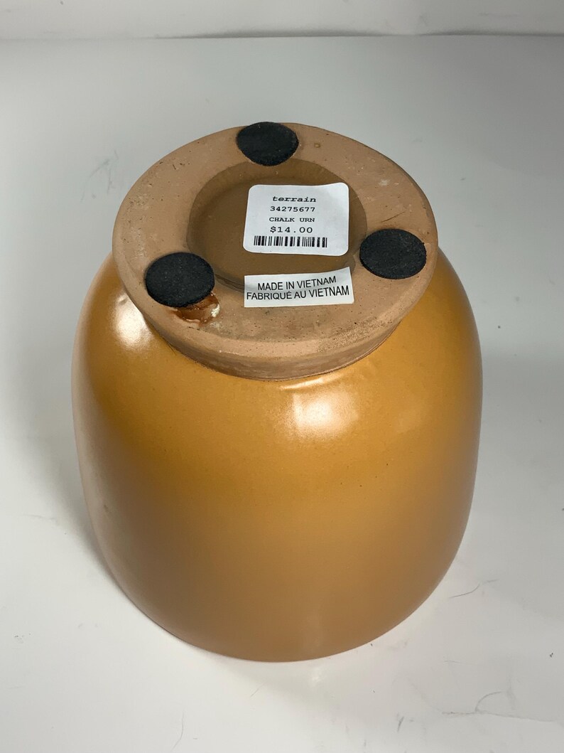Pu&ograve; includere: Un'urna in ceramica di colore terracotta con una base rotonda e un'ampia apertura. L'urna ha un'etichetta sul fondo che recita "terrain 34275677 CHALK URN 14,00 &euro;" e "MADE IN VIETNAM FABRIQUE AU VIETNAM".