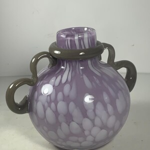 May include: A purple glass vase with white speckles and a grey rim. The vase has two grey handles.