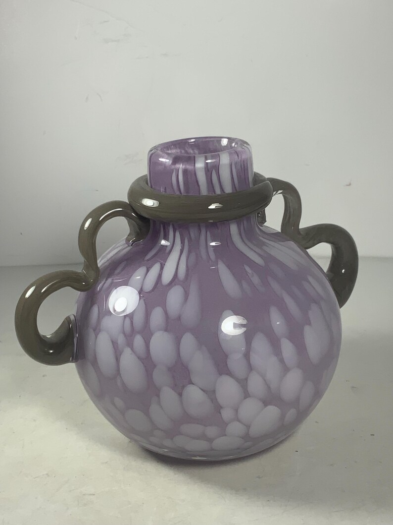 May include: A purple glass vase with white speckles and a grey rim. The vase has two grey handles.