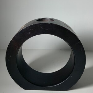 Puede incluir: Un jarr&oacute;n de madera negro en forma de anillo con un peque&ntilde;o agujero en la parte superior. El jarr&oacute;n est&aacute; hecho de madera oscura y tiene un acabado liso y pulido.