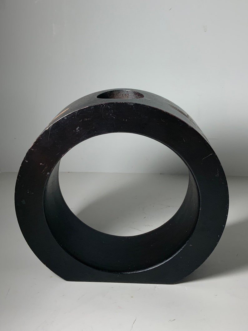 Puede incluir: Un jarr&oacute;n de madera negro en forma de anillo con un peque&ntilde;o agujero en la parte superior. El jarr&oacute;n est&aacute; hecho de madera oscura y tiene un acabado liso y pulido.