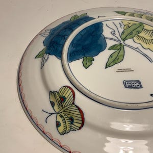 May include: White ceramic plate with a blue floral design and a yellow butterfly with red accents. The plate has a red scalloped border and the text "MOLLY HATCH".