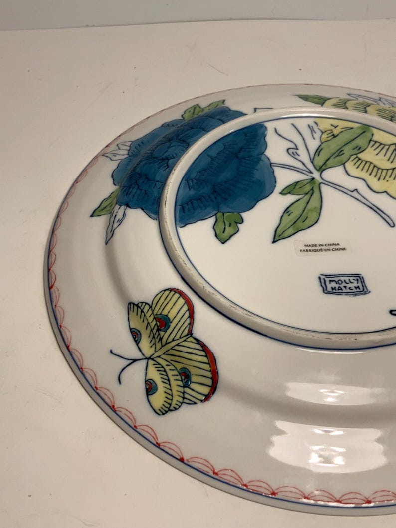 May include: White ceramic plate with a blue floral design and a yellow butterfly with red accents. The plate has a red scalloped border and the text "MOLLY HATCH".