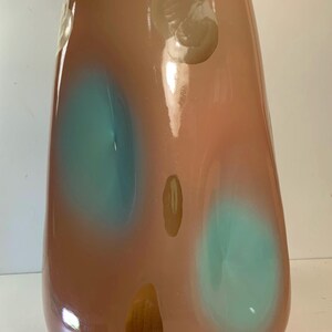 May include: A tall, teardrop-shaped glass vase in shades of peach and brown, with two large teal-colored spots and several smaller, lighter-colored spots. The vase has a glossy finish and a wide opening, suitable for floral arrangements.